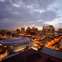 A panoramic view of a city skyline at dusk, with illuminated buildings and streets under a partly cloudy sky.